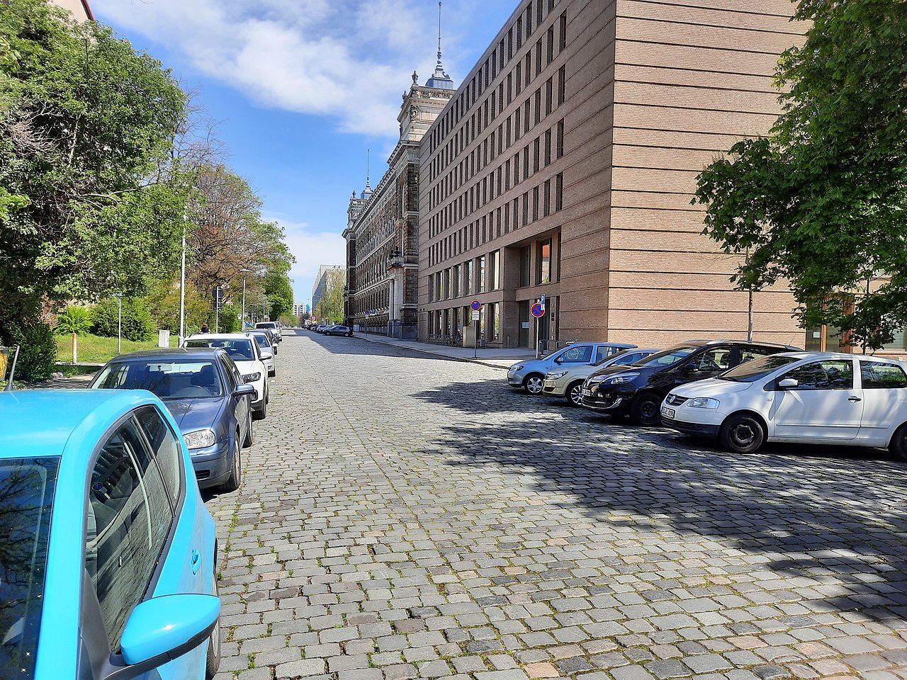 Eine Straße mit Bäumen und parkenden Autos. Im Hintergrund, der Neubau des Amtsgericht Dresden, sowie der Altbau vom Landgericht.