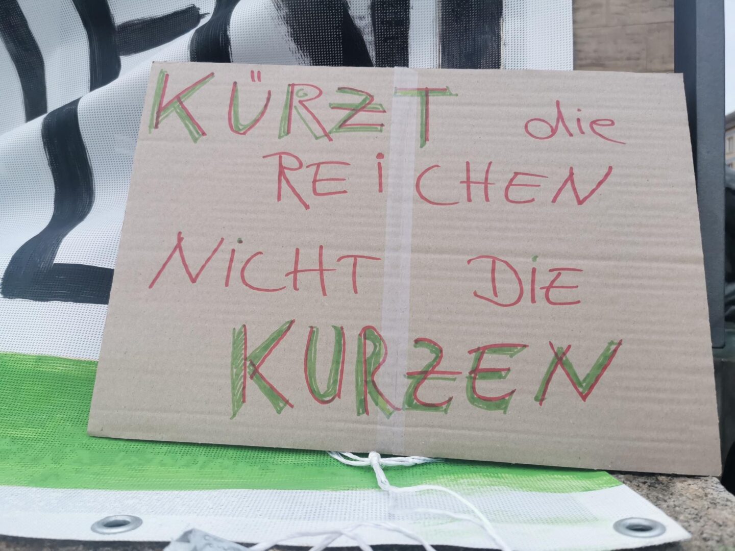 Pappschild mit der Aufschrift "Kürzt die Reichen nicht die Kurzen"